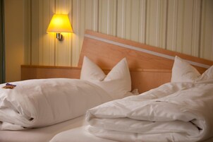 Quarto de hotel com cabeceira de madeira, roupa de cama branca e luminária fixada na parede.