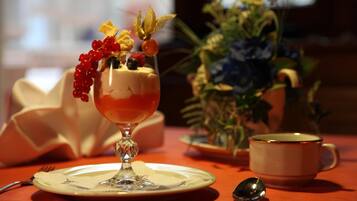 Dessert i et glas på en tallerken, en kop og en ske på et bord med en plante i baggrunden.