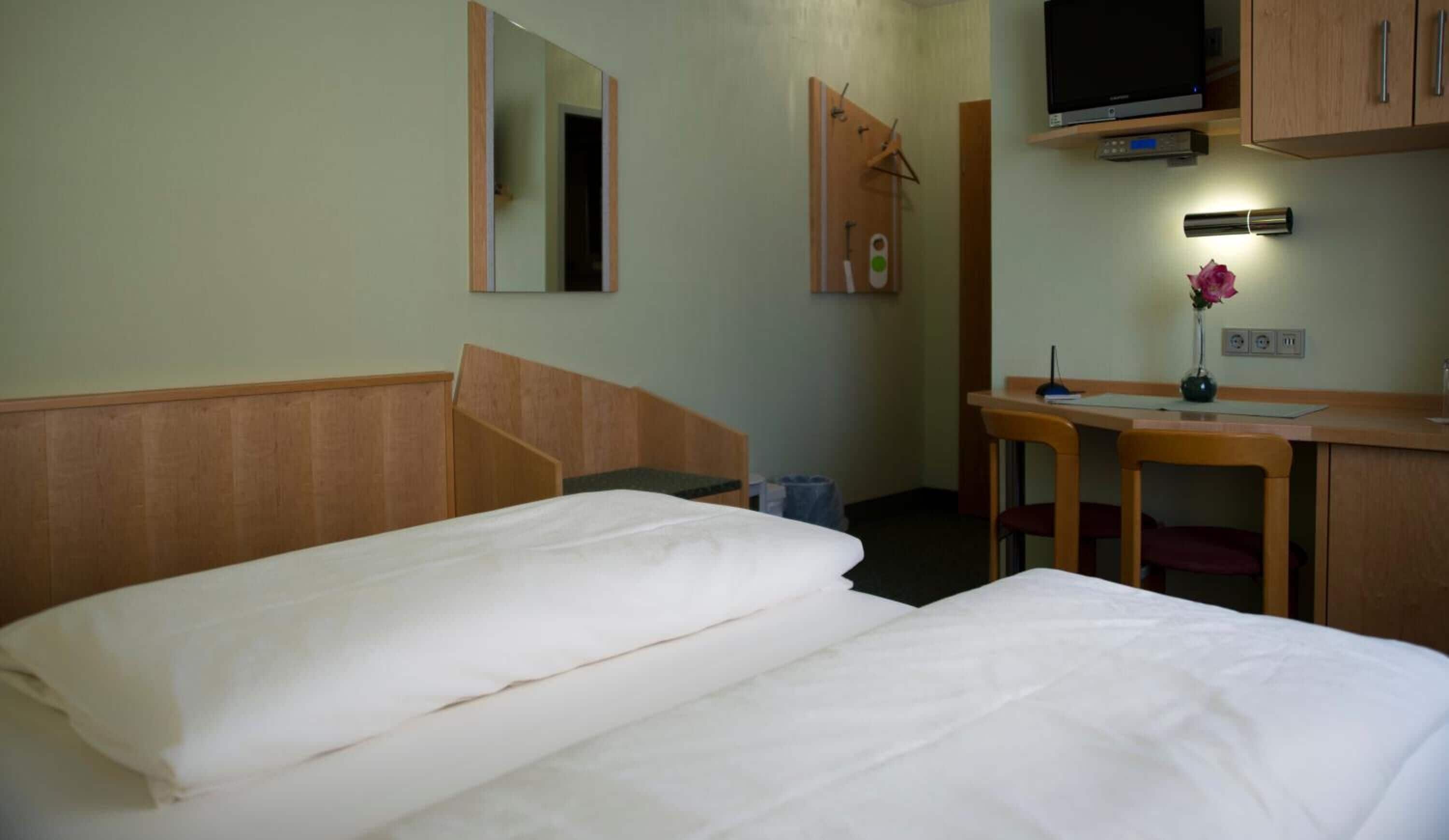 A hotel room with two beds, a desk with a chair, a television, and a mirror.