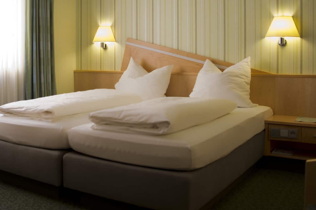 Un lit double avec deux oreillers et du linge de lit blanc plié, une tête de lit en bois et deux lampes de chevet.