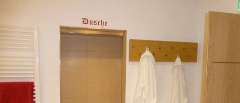A bathroom with a shower, a towel rack with white towels, and a wooden door.