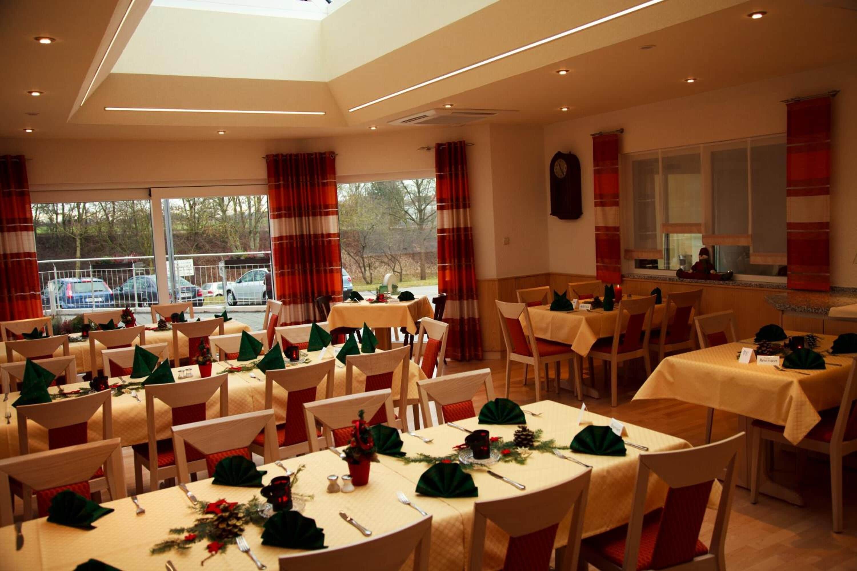A dining area with multiple tables set for a meal, featuring green centerpieces and red and white striped curtains.