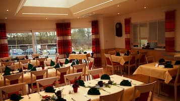 A dining area with multiple tables set for a meal, featuring green centerpieces and red and white striped curtains.