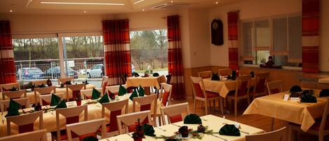 A dining area with multiple tables set for a meal, featuring green centerpieces and red and white striped curtains.