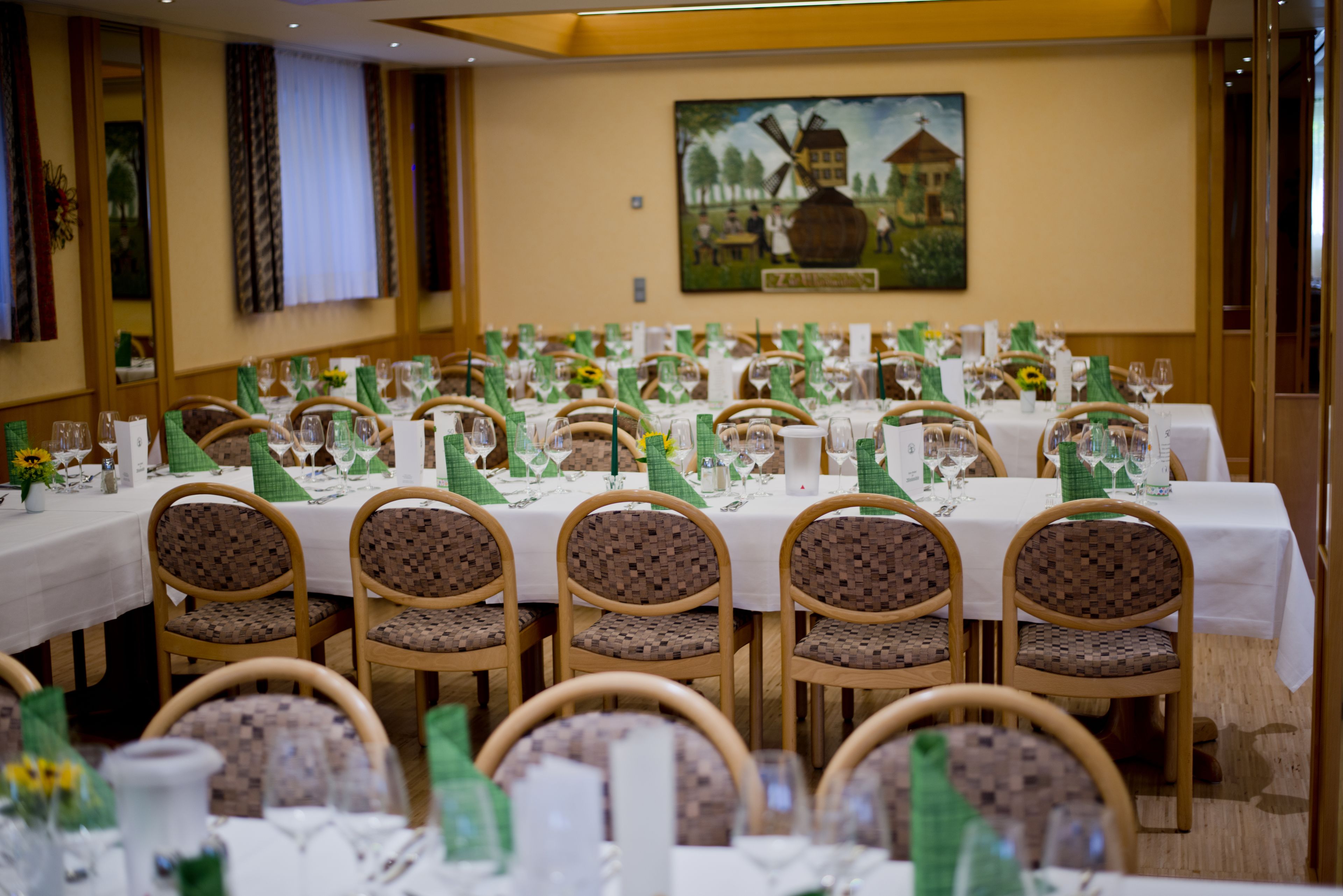 A banquet hall with multiple round tables set for dining, each with green tablecloths and white centerpieces.