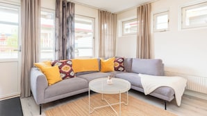 A modern living room with a grey sofa, yellow cushions, a round coffee table, and a view of the outside through large windows. - Åre Travel - Center (Are)