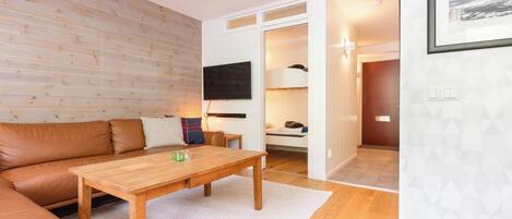Una sala de estar acogedora con piso de madera, un sofá de cuero marrón, una mesa de centro de madera y una pared blanca con un diseño geométrico.