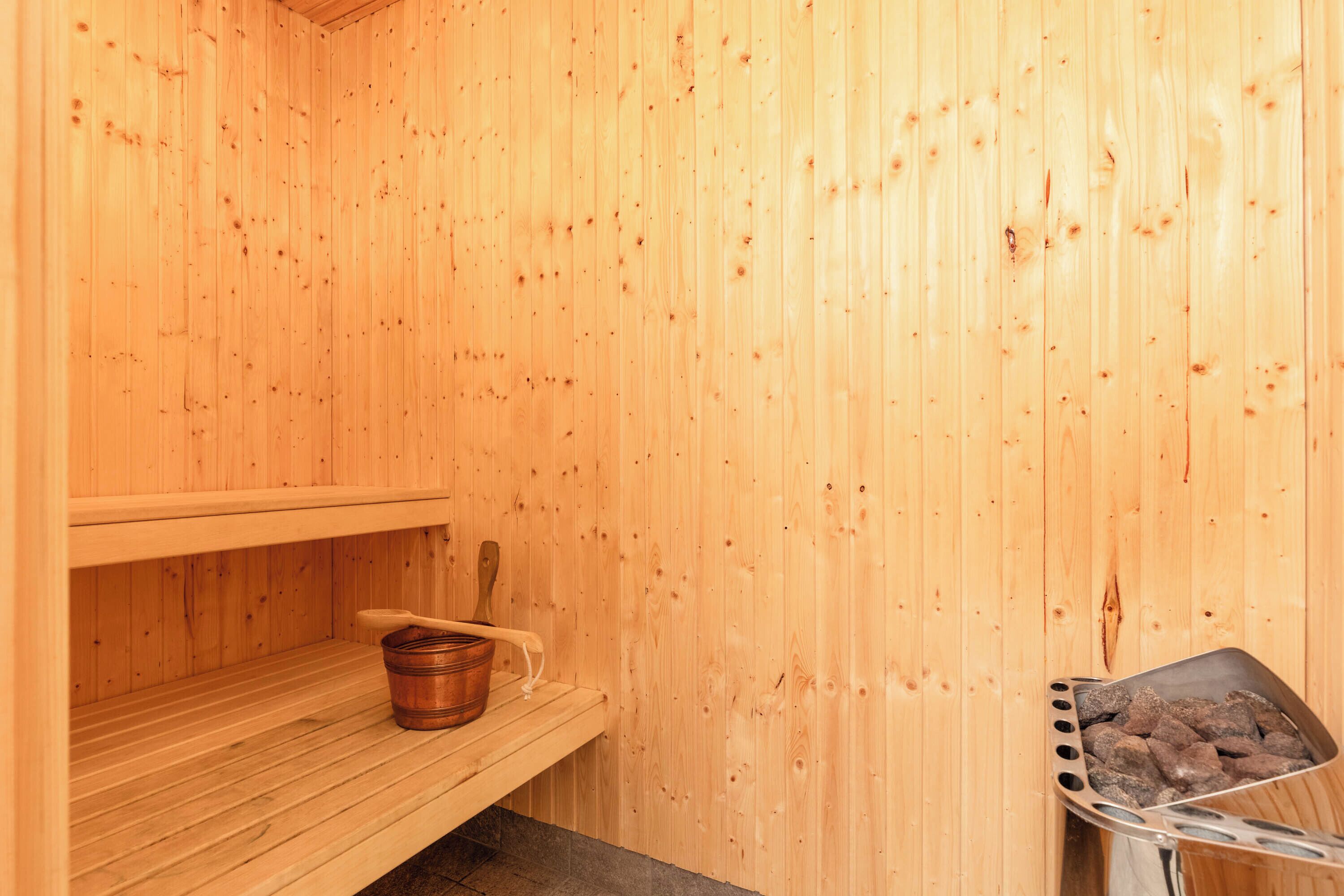 A wooden sauna with a bench, a bucket, and a tray of rocks.