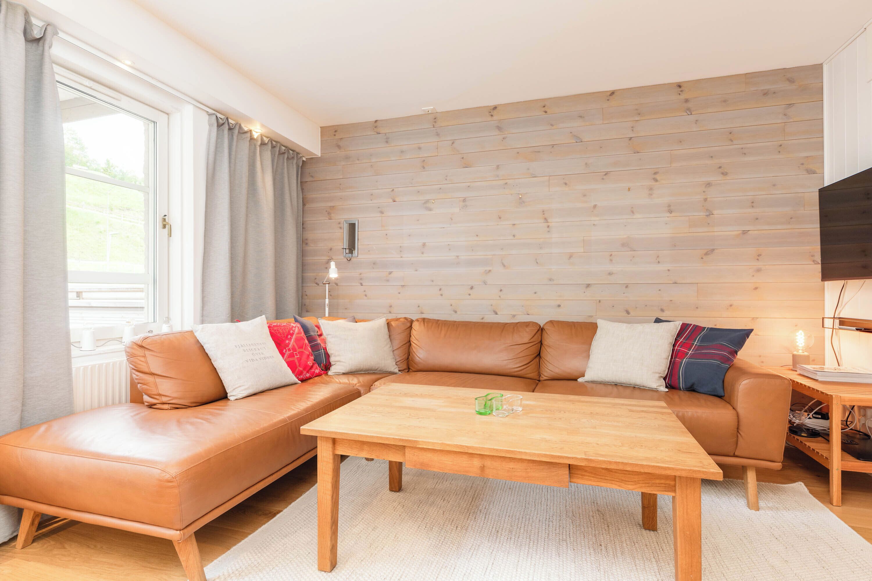 A modern living room with a sectional sofa, a wooden coffee table, and a TV on a wooden wall.