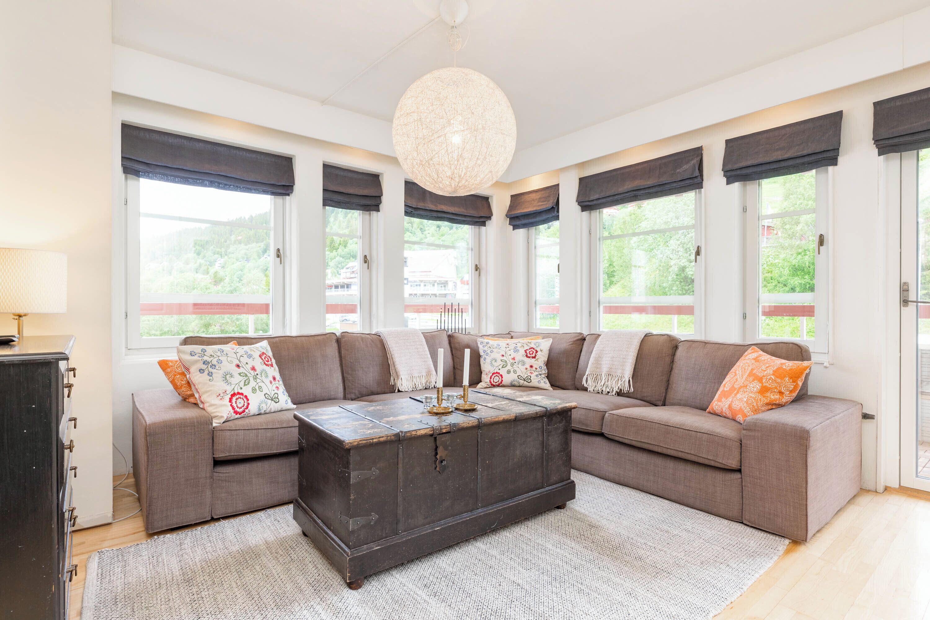 Ein modernes Wohnzimmer mit einem Ecksofa, einem dunkelholznen Couchtisch und großen Fenstern mit dunklen Vorhängen.
