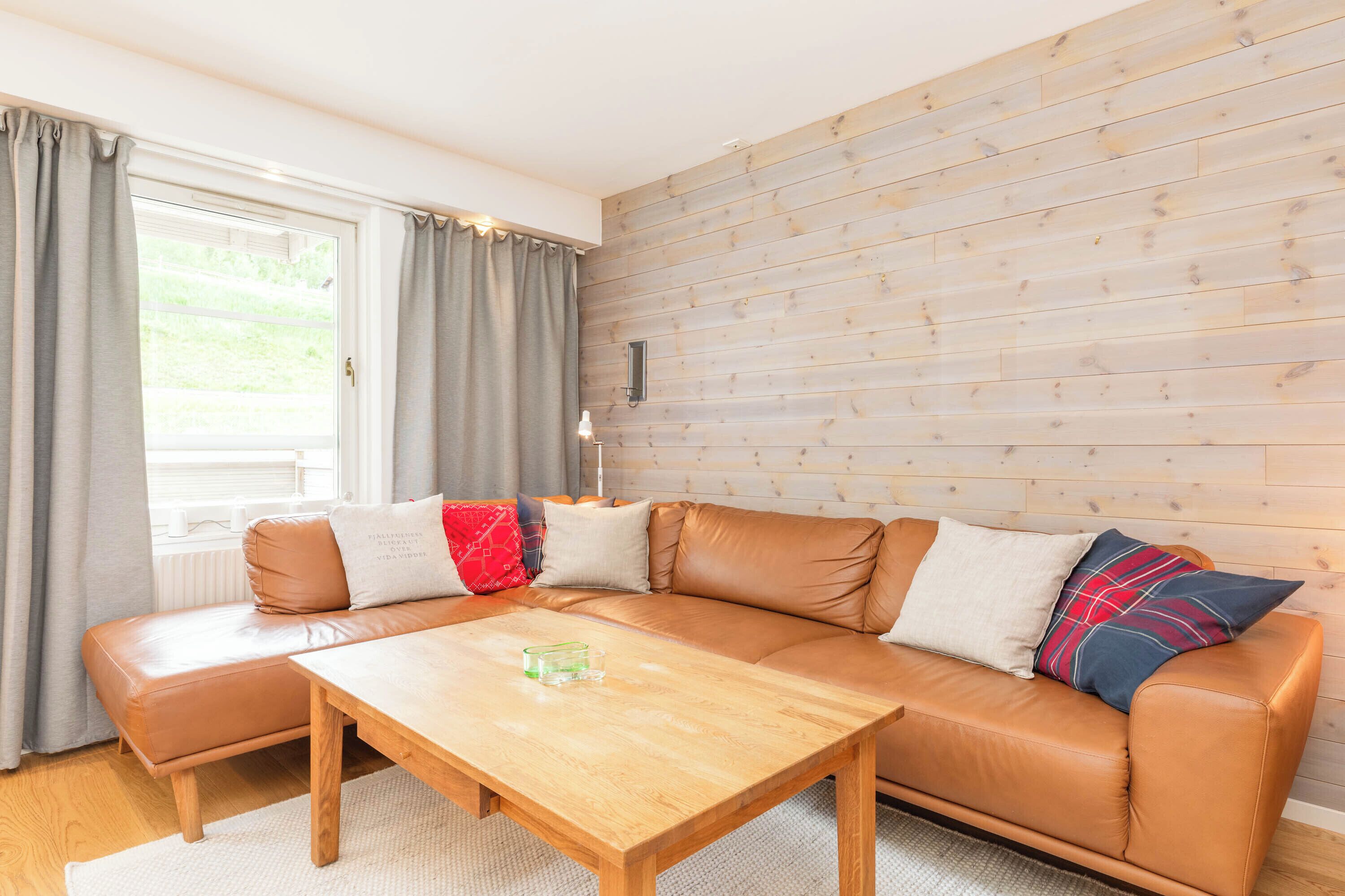 Una sala de estar con un sofá de cuero marrón, una mesa de centro de madera y un ventanal con cortinas.