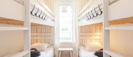 A room with bunk beds, a small table, and a window with curtains.