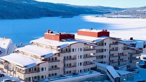 A modern multi-story hotel with a flat roof, located near a frozen lake with a forested backdrop. - Åre Travel - Center (Are)