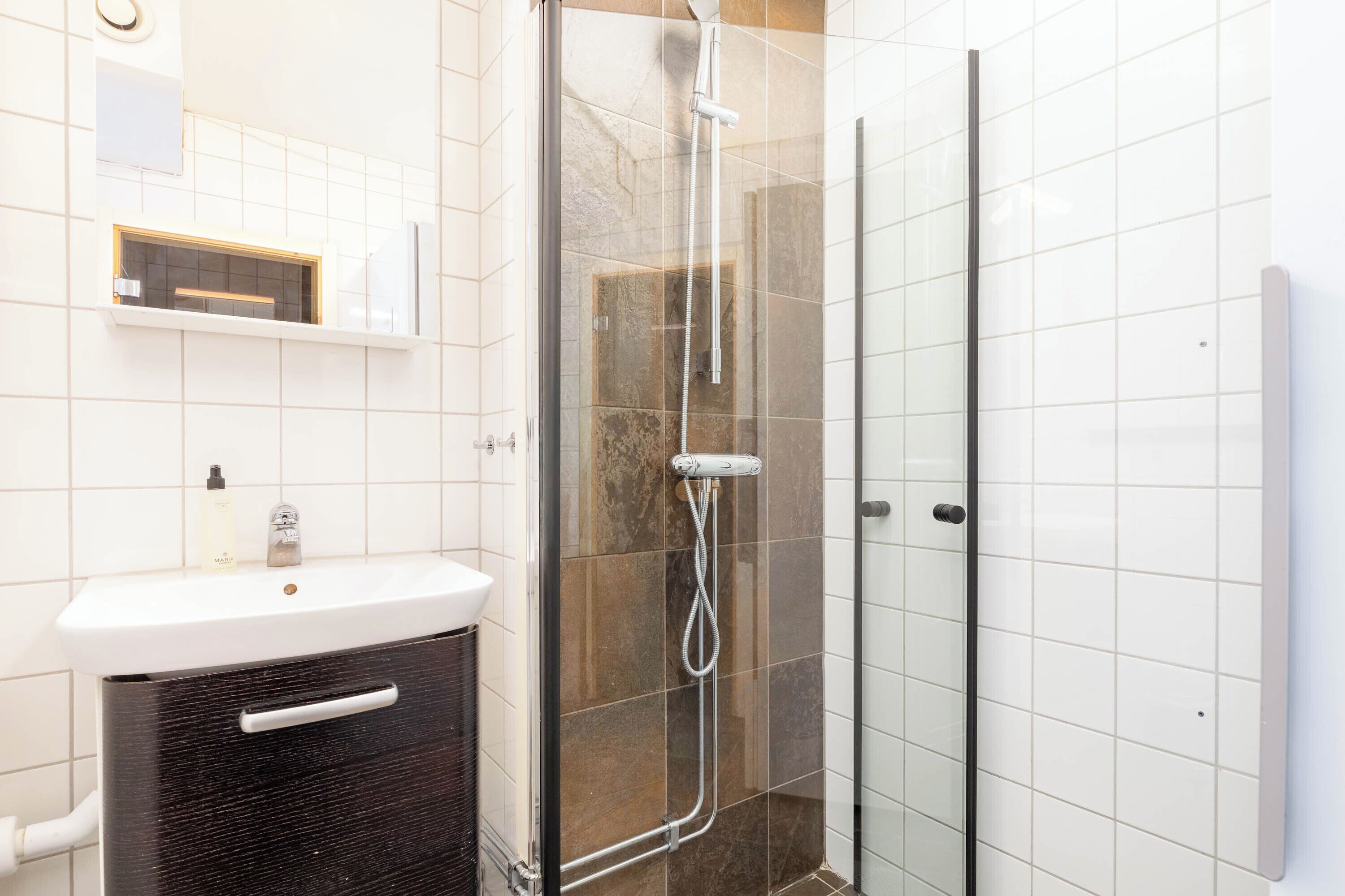 Une salle de bain avec une douche à parois de verre, un lavabo blanc et un meuble noir.
