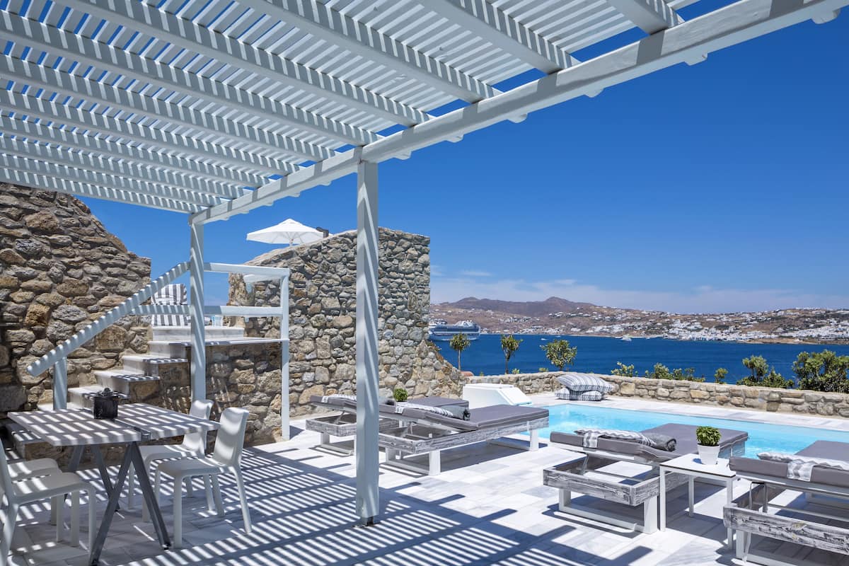 Ein Poolbereich mit weißer Möbel, einer Steinwand und Blick auf das Meer.