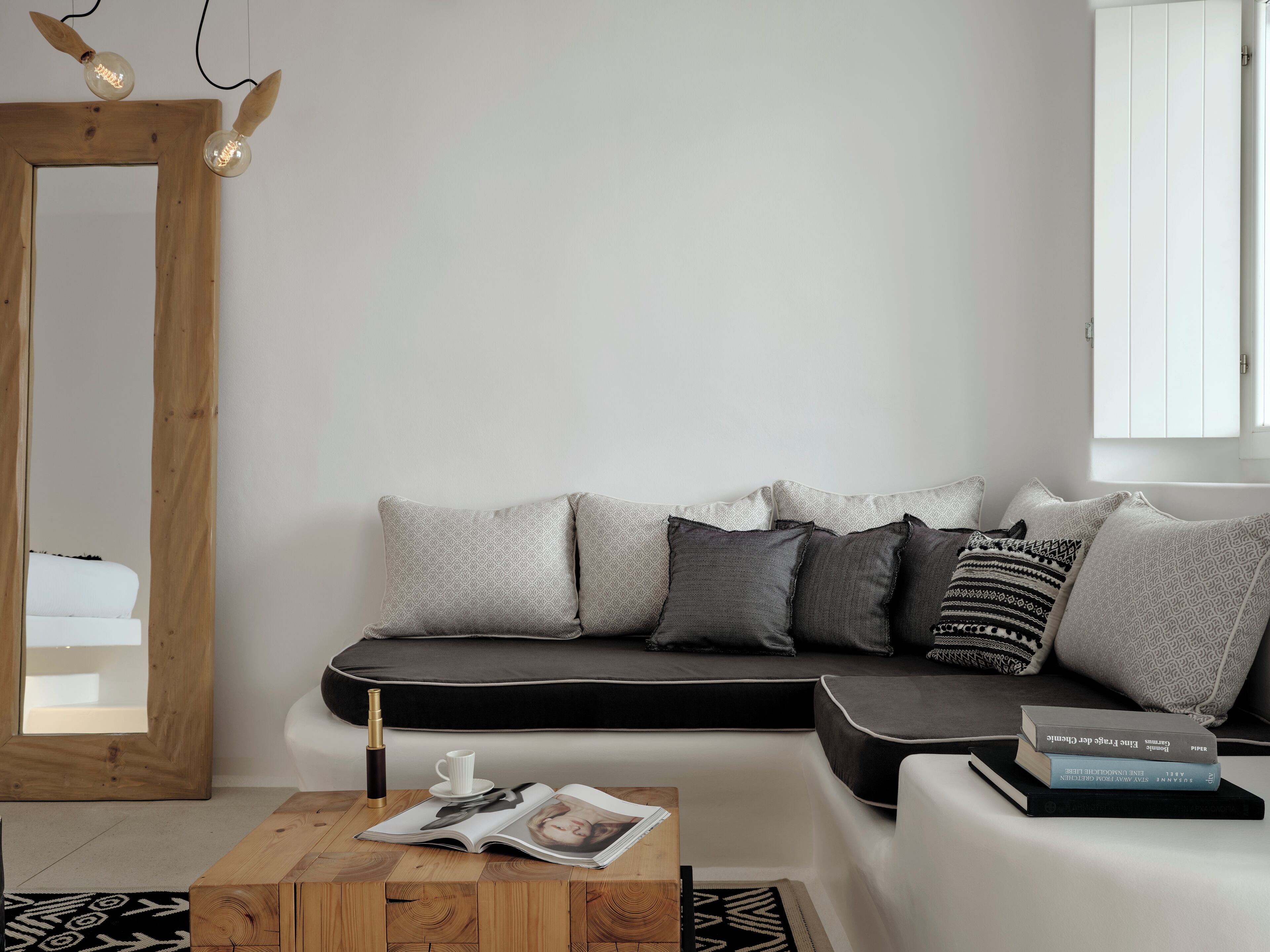 Een moderne woonkamer met een spiegel met houten lijst, een bank met kussens met dessin, een bijzettafeltje met een tijdschrift en een boek.