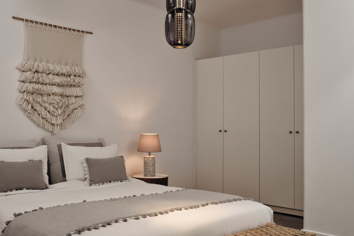 Ein Schlafzimmer mit Bett, Nachttischlampe, Kleiderschrank und einem gewebten Hocker.