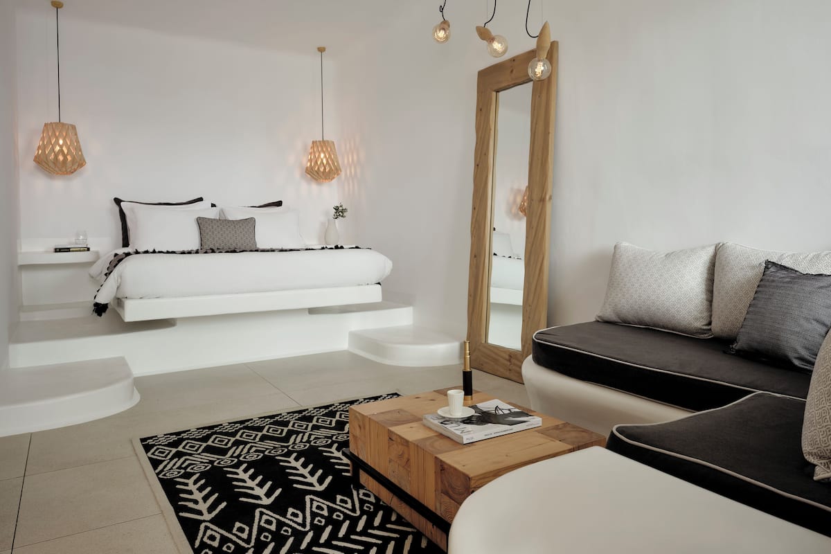 Ein modernes Schlafzimmer mit einem weißen Bett, einem hölzernen Nachttisch, einem schwarz-weißen Teppich, einem Holztisch und einem großen Spiegel.