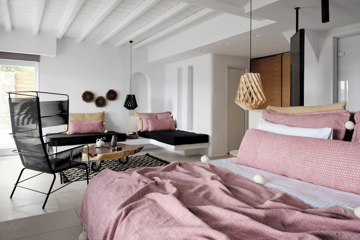 Ein modernes Schlafzimmer mit einem großen Bett, einer Sitzecke mit Sofa und Sessel sowie einem Esstisch.