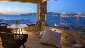 A stone-walled terrace with a round table and chairs, a view of the sea, and a cityscape in the distance. - Mykonos No5 (Mykonos)
