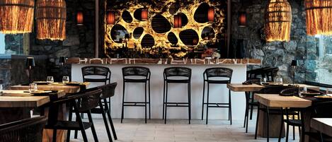 Interior de restaurante con pared de piedra, lámparas colgantes y zona de bar.