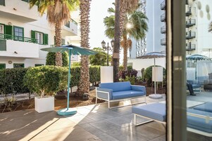 Un espace extérieur aménagé avec un canapé bleu, une table blanche et un parasol bleu.