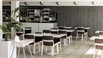 Un restaurante moderno con mesas y sillas blancas, una cafetera y una planta en maceta.