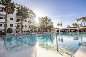 A pool area with lounge chairs and palm trees, surrounded by a multi-story building with balconies. - Servatur Playa Bonita (San Bartolomé de Tirajana)