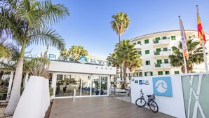 A hotel entrance with a modern design, palm trees, and a bicycle parked outside. - Servatur Playa Bonita (San Bartolomé de Tirajana)