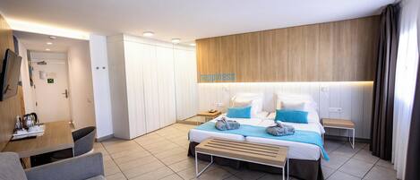 A modern hotel room with a bed, a desk, a chair, and a wardrobe.