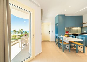 A modern kitchen with blue cabinets, a dining table with chairs, and a view of the sea through a sliding door. - Georgina (Chania)