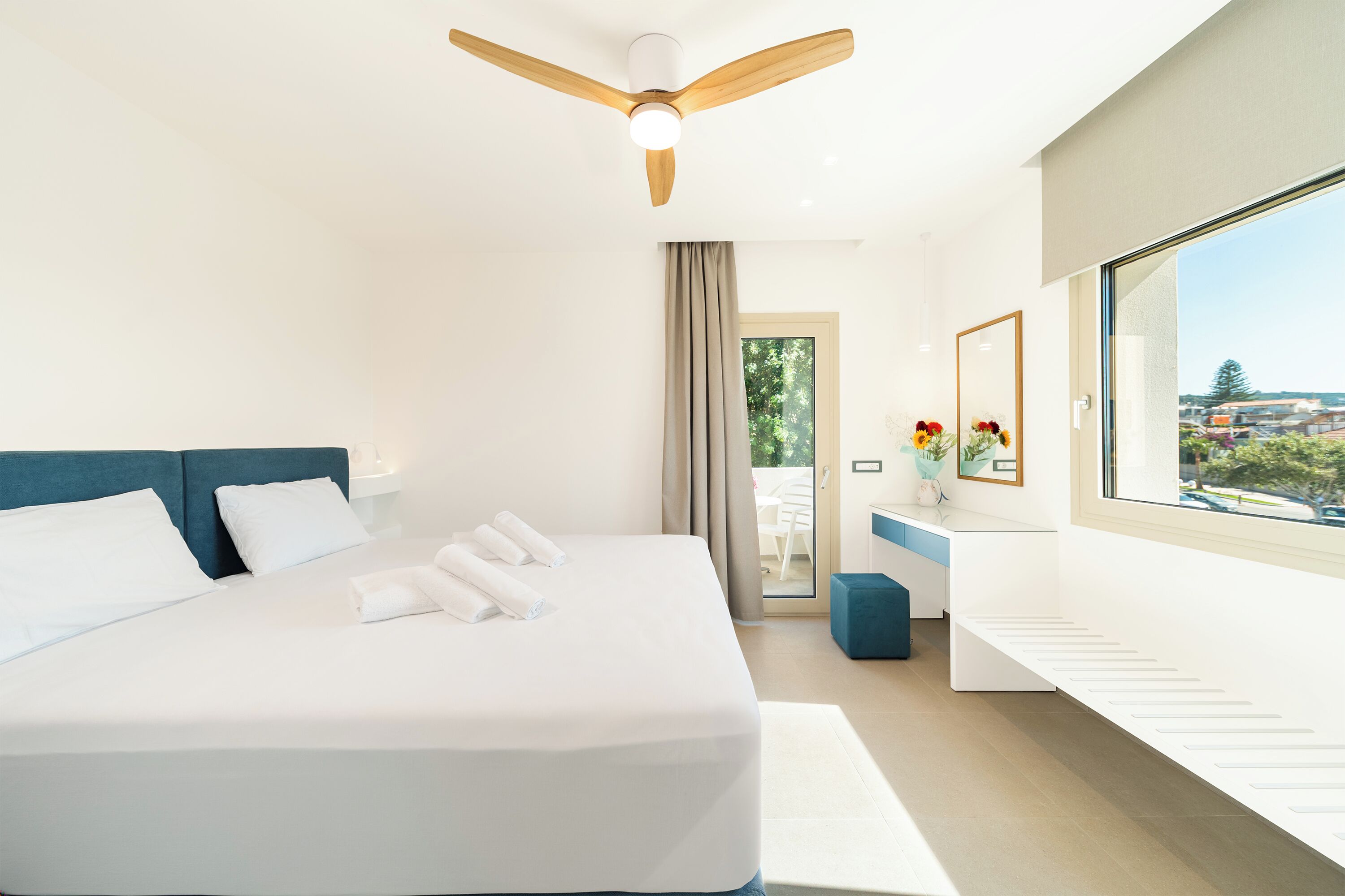 A modern hotel room with a large bed, a ceiling fan, a view of the outdoors, and a small desk area.
