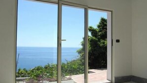 Une pièce dotée d’une porte-fenêtre coulissante donnant sur un balcon avec vue sur la mer et la verdure.