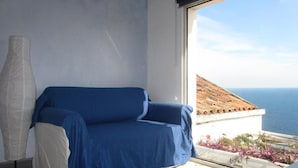 Une pièce avec un canapé bleu, un lampadaire blanc et une vue sur la mer par une fenêtre.