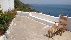 Un balcon avec une chaise en bois, des murs blancs et une vue sur la mer.