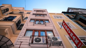 Um edifício com várias andares, varandas, aparelhos de ar condicionado e uma placa vermelha com texto branco.