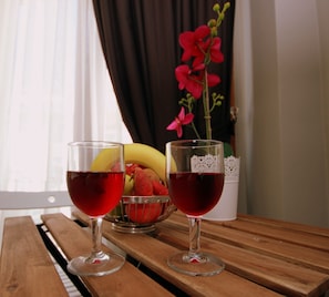 Two glasses of red wine on a wooden table with a bowl of fruit and a vase of flowers in the background. - Ada House Oldcity (Istanbul)