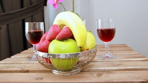 Uma tigela de frutas com bananas, morangos e uma maçã sobre uma mesa de madeira, acompanhada de dois copos de vinho tinto.