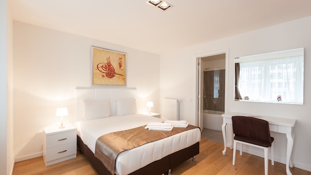 Quarto com cama, mesas de cabeceira, escrivaninha e uma cadeira.