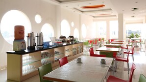 Un espace repas lumineux, doté de fenêtres rondes, d’un comptoir avec des machines à café et de tables avec des chaises.