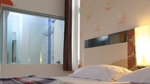 Une chambre d’hôtel avec une grande fenêtre, une douche et un lit avec du linge de lit blanc.