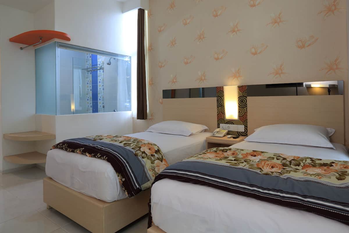 Une chambre d’hôtel avec deux lits, une salle de bain avec douche et un mur décoré de motifs.