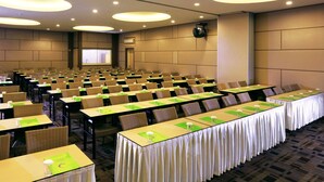 Une salle de conférence avec des rangées de tables et de chaises, équipée de projecteurs et d’écrans.