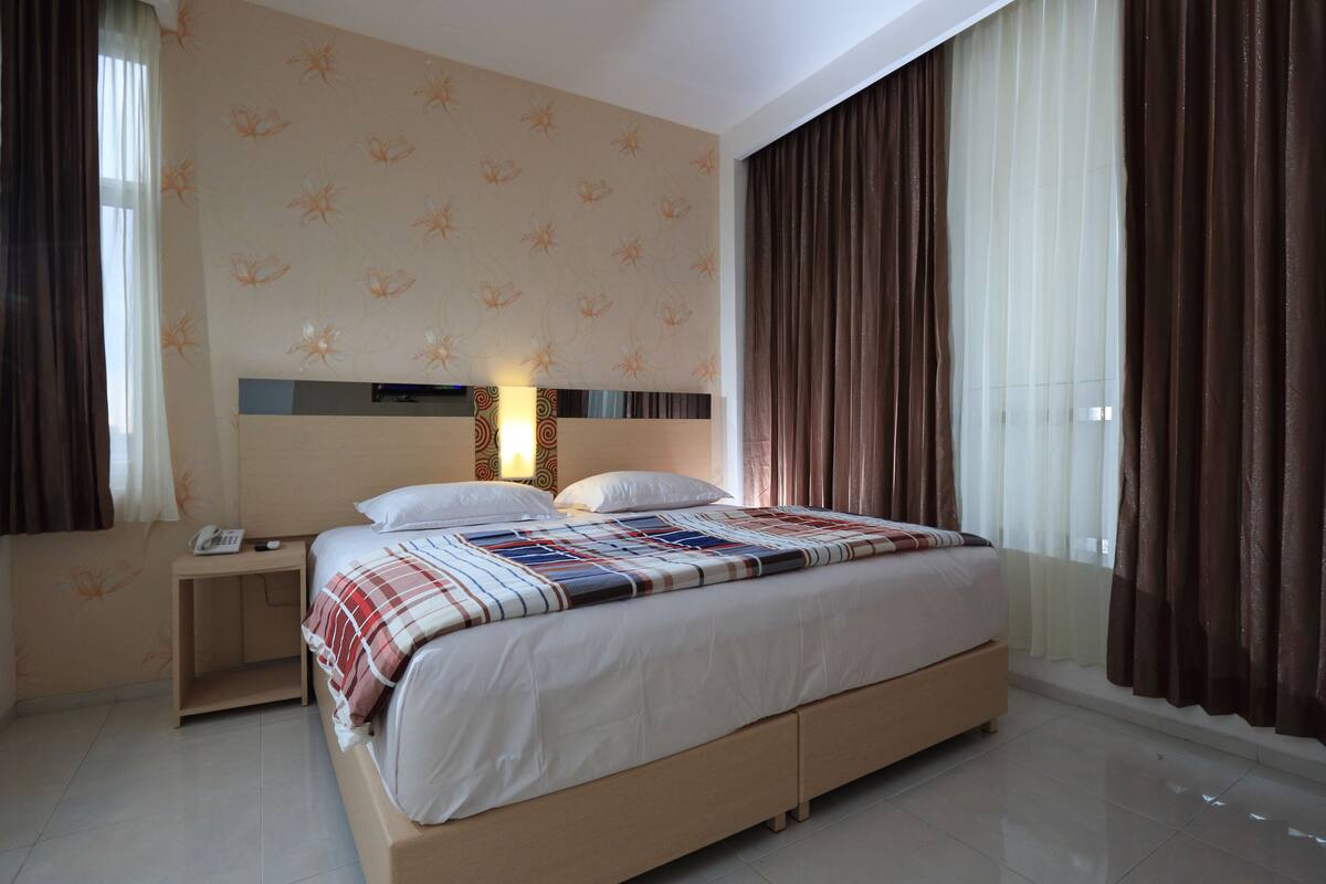 Une chambre d’hôtel avec un grand lit, une table de chevet avec un téléphone et une petite table de nuit.
