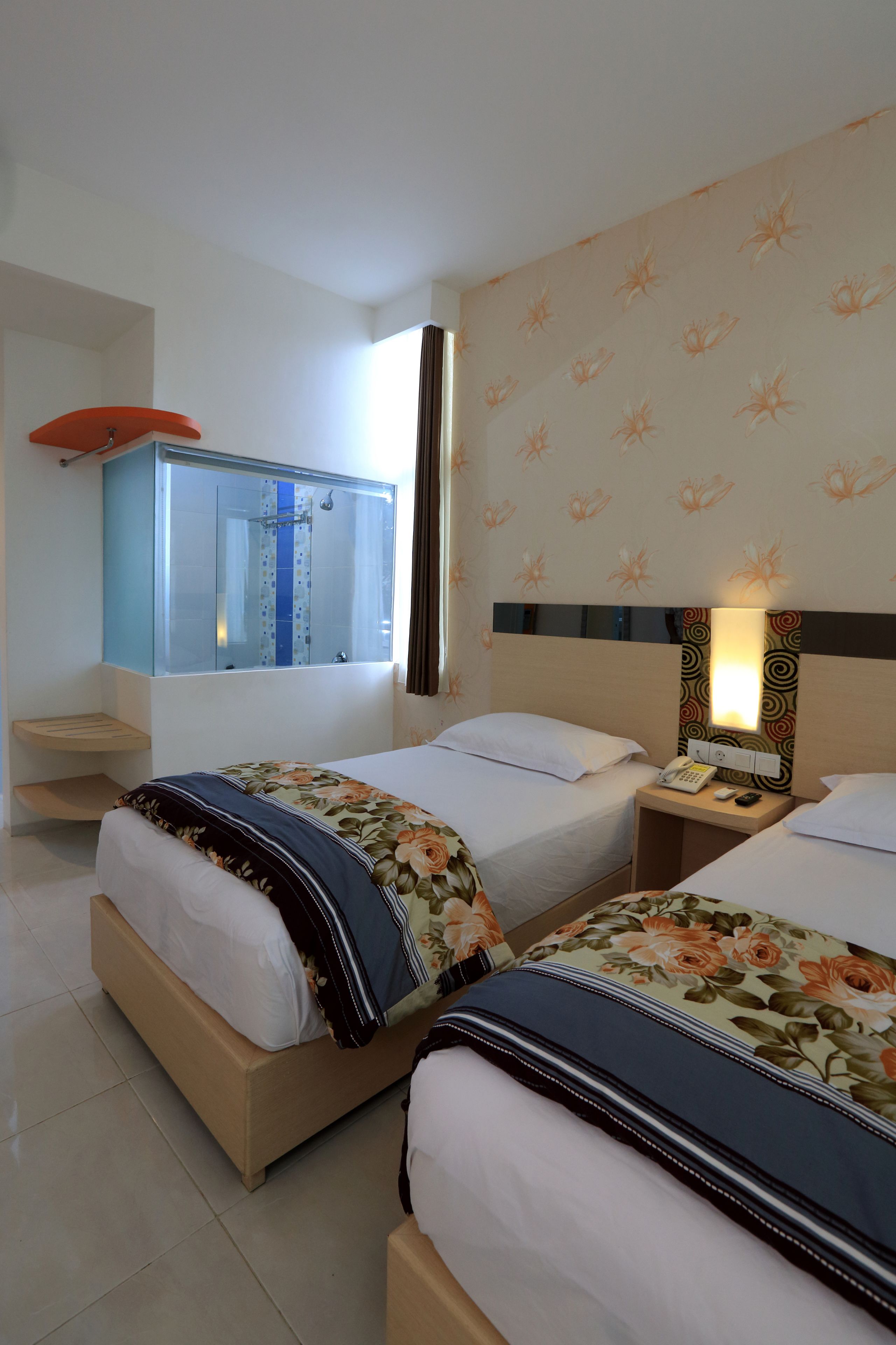 A hotel room with two beds, a bathroom with a shower, a nightstand with a lamp, and a mirror above the bed.