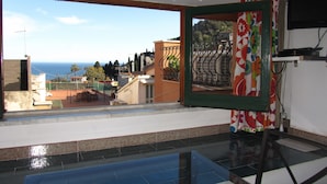 A room with a large window offering a view of the sea and buildings. - Come In Sicily - Al Mercato (Taormina)