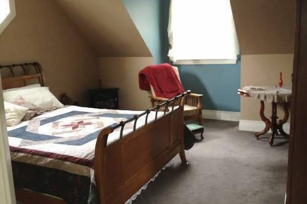 Une chambre à coucher avec un lit en bois, une chaise, une petite table et une fenêtre.
