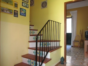 Un escalier avec une rampe noire, des murs jaunes et des carreaux décoratifs.