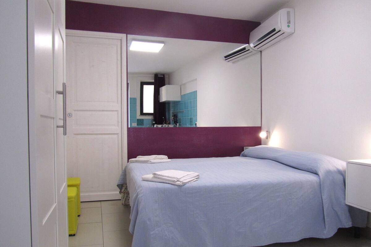 A bedroom with a bed, a wardrobe, a mirror, and an air conditioning unit.
