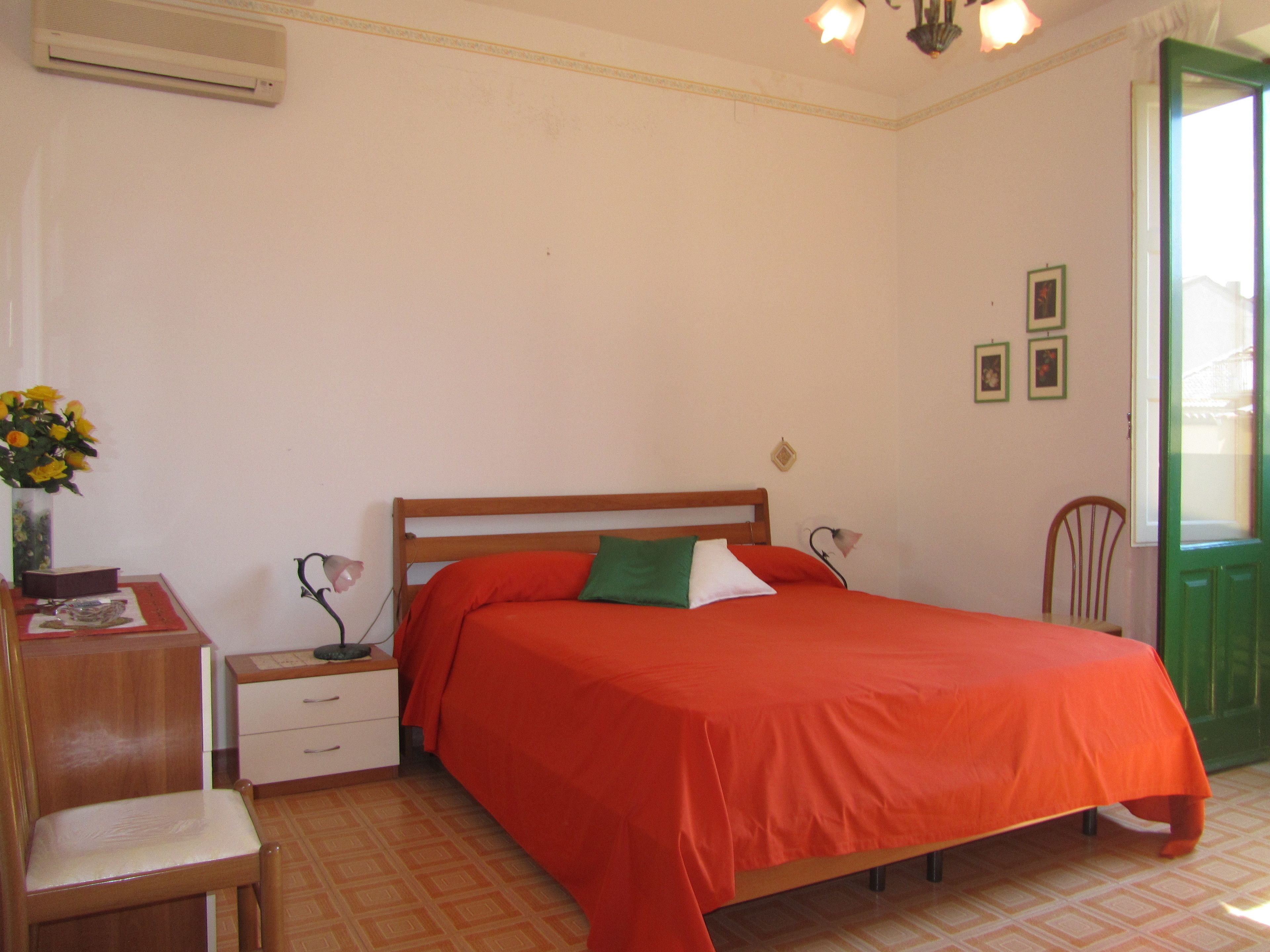 A bedroom with a single bed, a bedside table, a chair, and a small table with a vase of flowers.